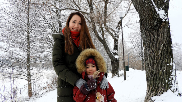 Inabat and her child are posing in their winter outfit in a snowy park.