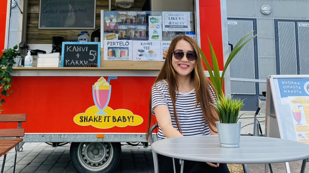 A woman is sitting at an outdoor café table, smiling.