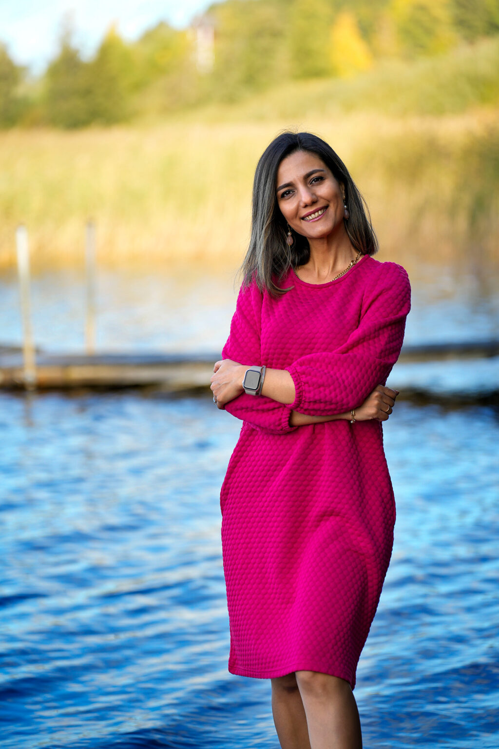 Parastoo is standing close by a lake and smiling.