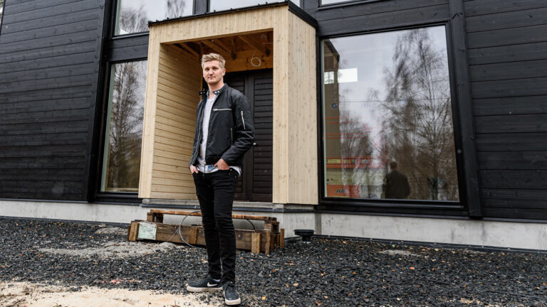 Young man stands in front of a modern black house.