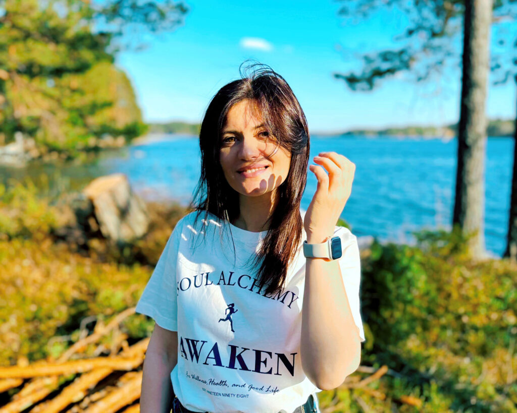 A woman smiles at the camera. A sunny and warm summer day, with a lake view in the background.